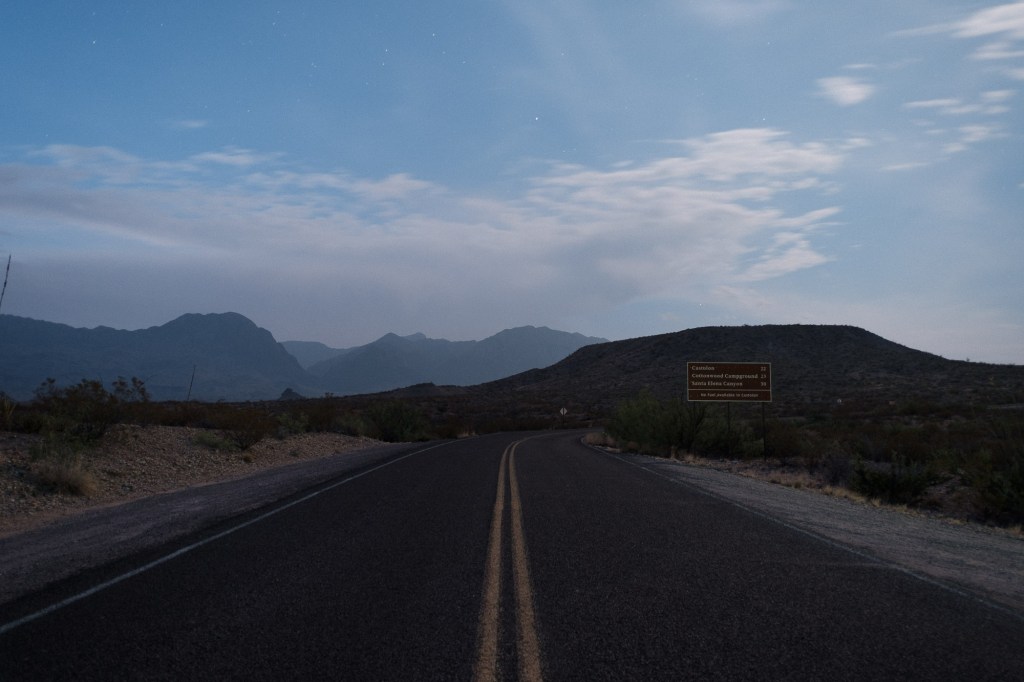 Early morning blue hour view standing in the middle of Ross Maxwell Scenic Drive, with the road leading toward distant mountains.