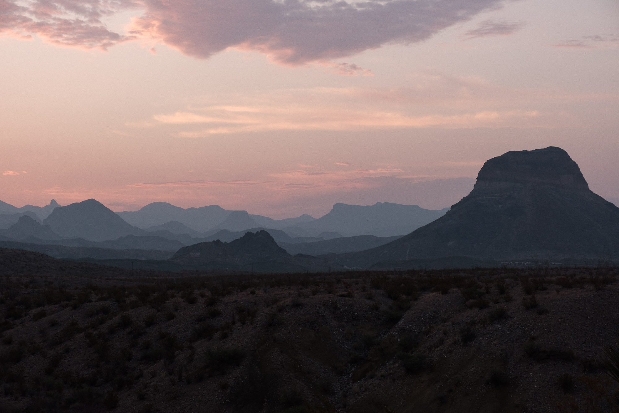 Pink-hued blue hour sky over layered silhouettes of mountains in Big Bend National Park.